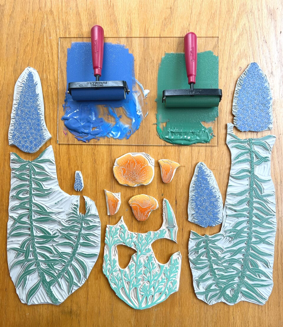 linocut printing blocks carved into lupines or similar flowers, with rolls of blue and green ink ready for printing